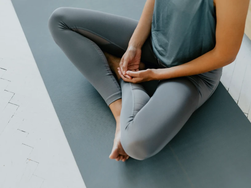 Person im Schneidersitz (Sukhasana) auf einer grauen Matte.