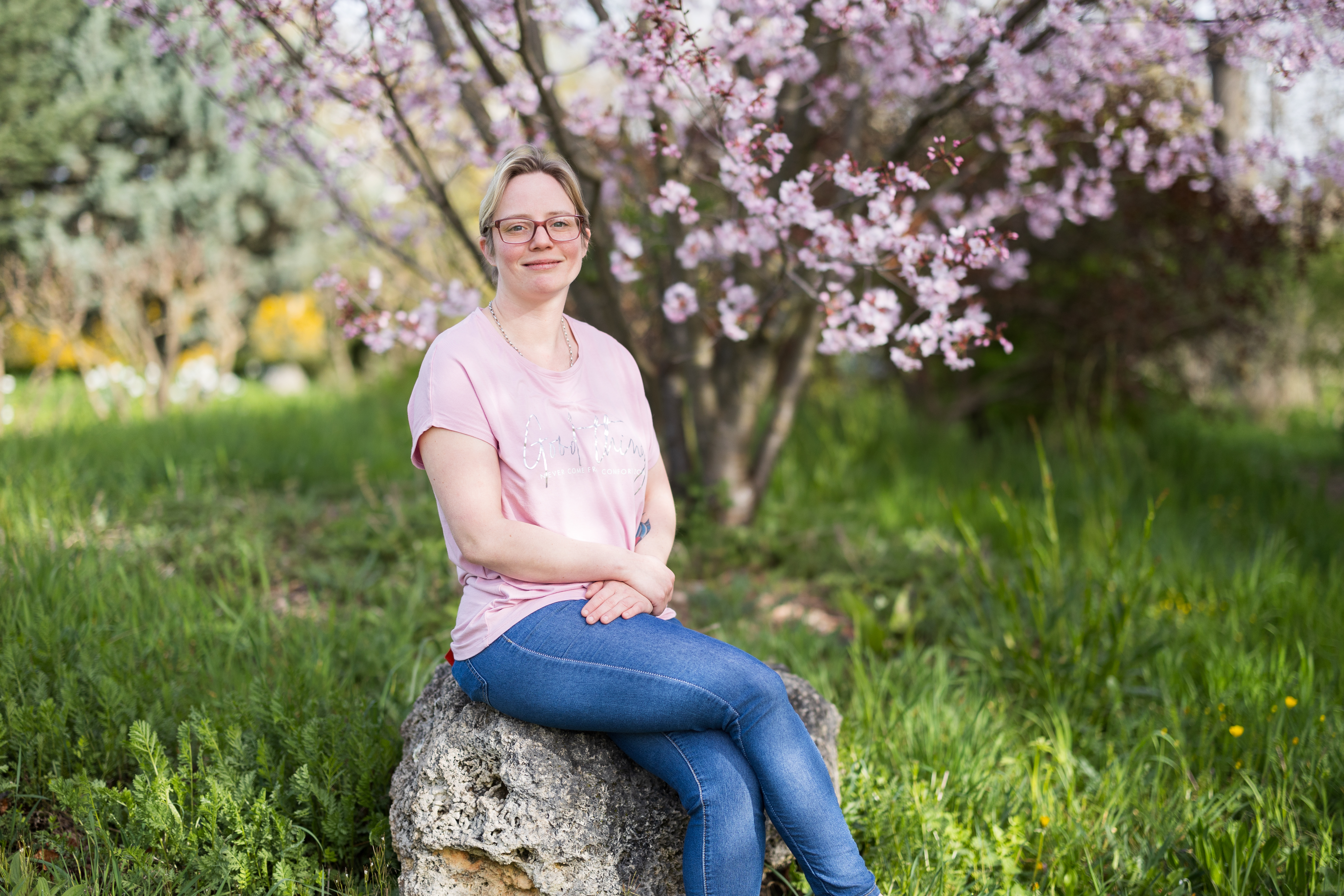 Bild einer jungen Frau auf einem Stein sitzend vor einem Garten.